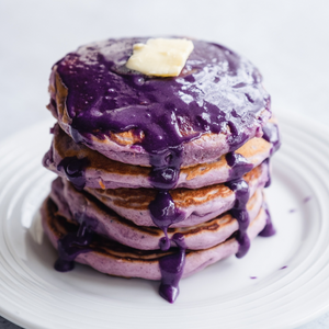 A stack of ube pancakes with ube cookie butter sauce and a pat of butter